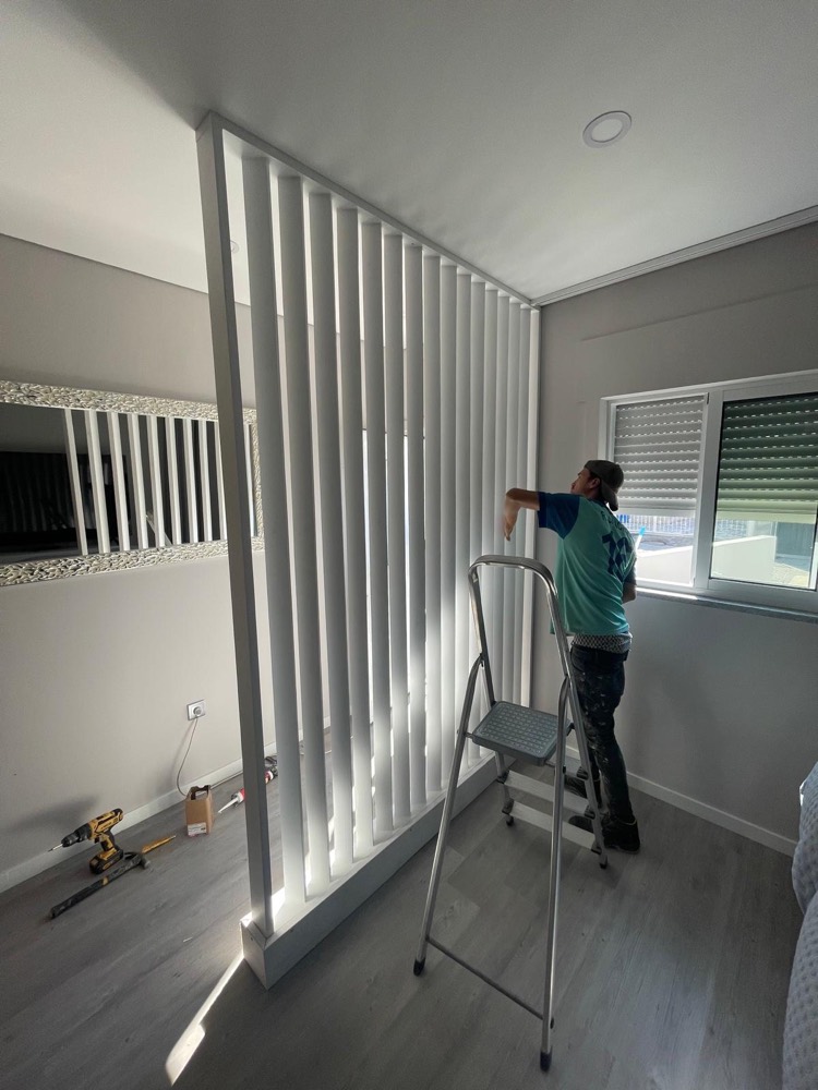 Membro da equipa num escadote a montar uma divisória em ripado branco